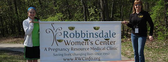 two women standing next to Robbinsdale Women's Center sign